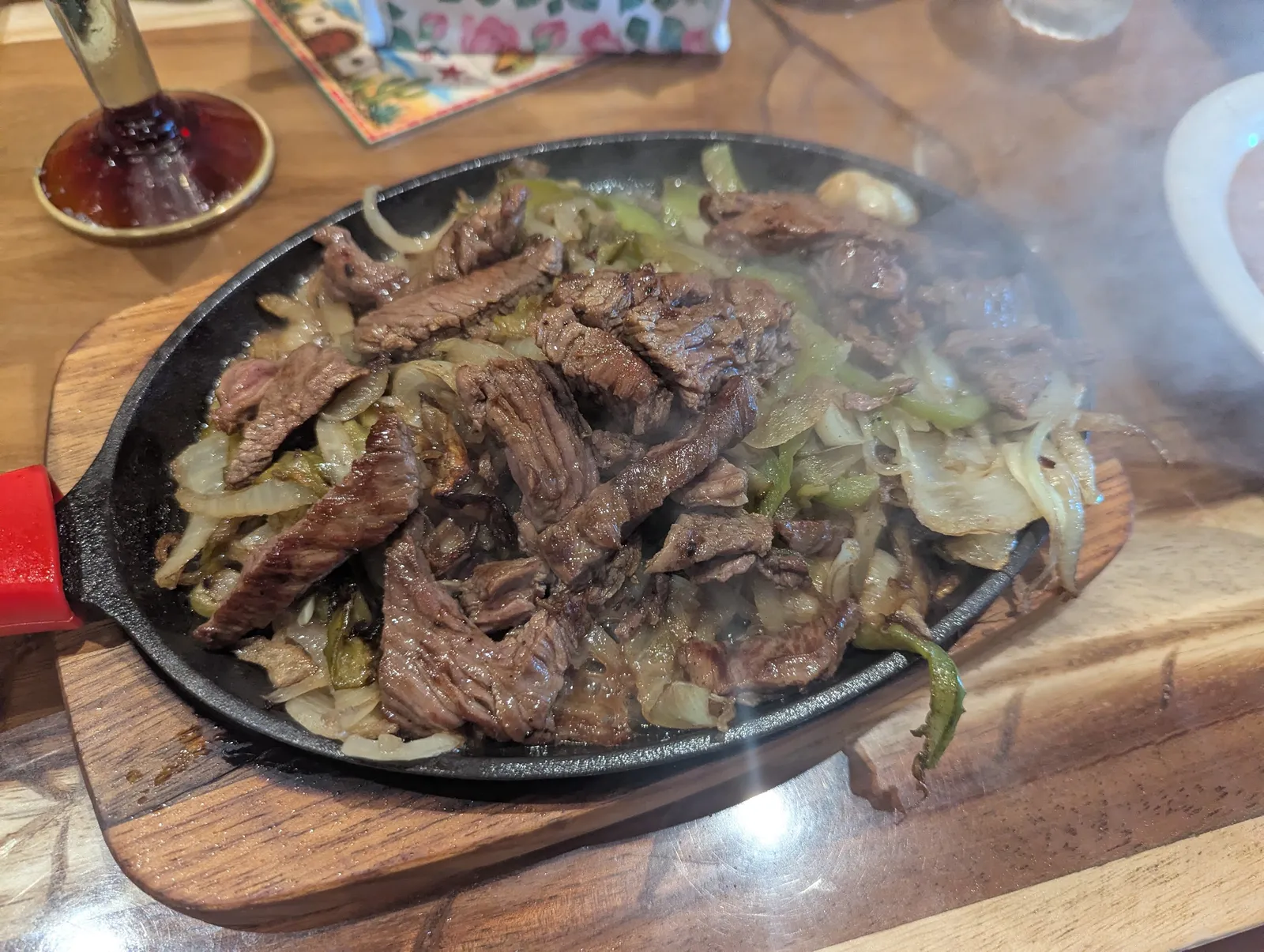 Steak fajitas with charred peppers and onions on a smoking cast-iron skillet