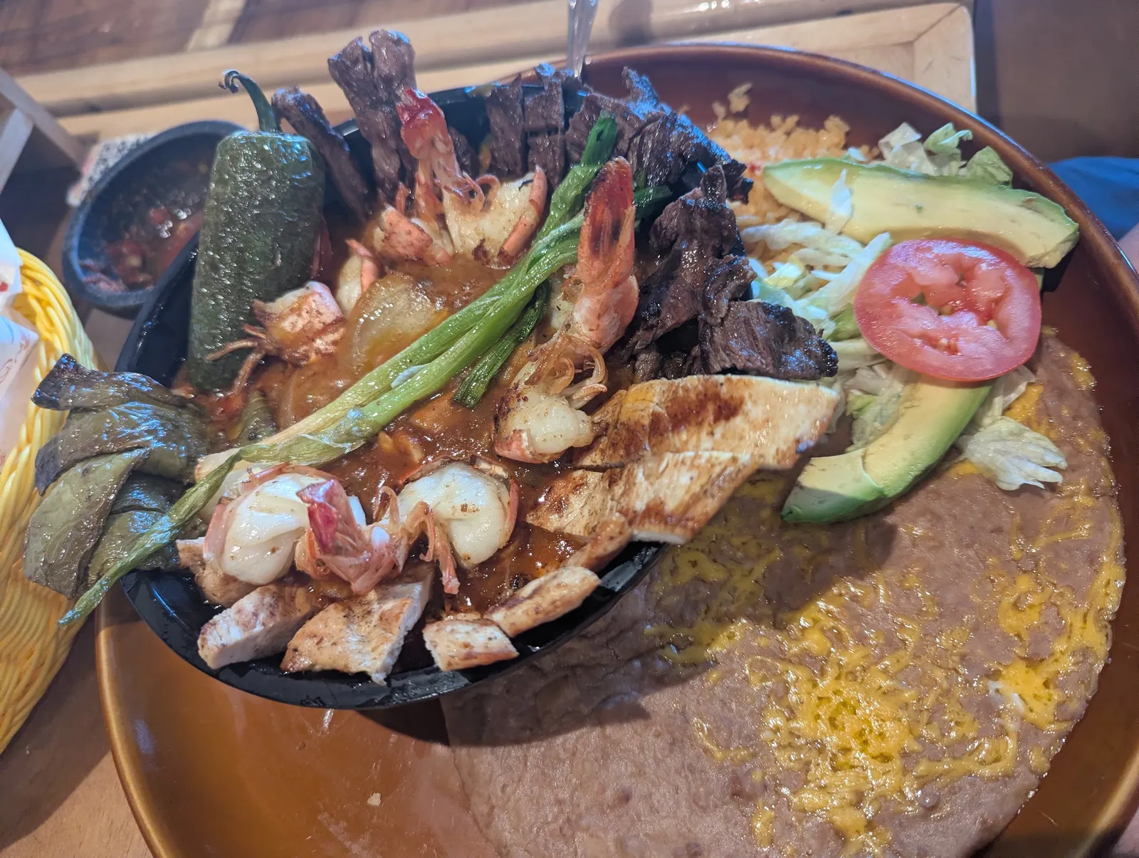 A sizzling stone molcajete of grilled steak, chicken, shrimp and nopal in red salsa
